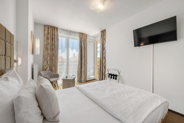 Una habitación de hotel con una cama grande, un televisor de pantalla plana montado en la pared, una silla y una mesita.