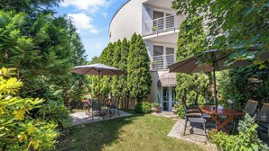 A courtyard with outdoor seating, surrounded by lush greenery and a building with a balcony. - Hotel ANTARES (Bratislava)