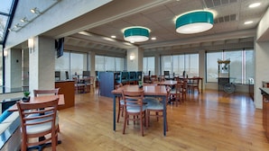 A spacious indoor area with multiple wooden tables and chairs, large windows, and a high ceiling with exposed beams.