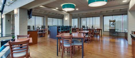 A spacious indoor area with multiple wooden tables and chairs, large windows, and a high ceiling with exposed beams.