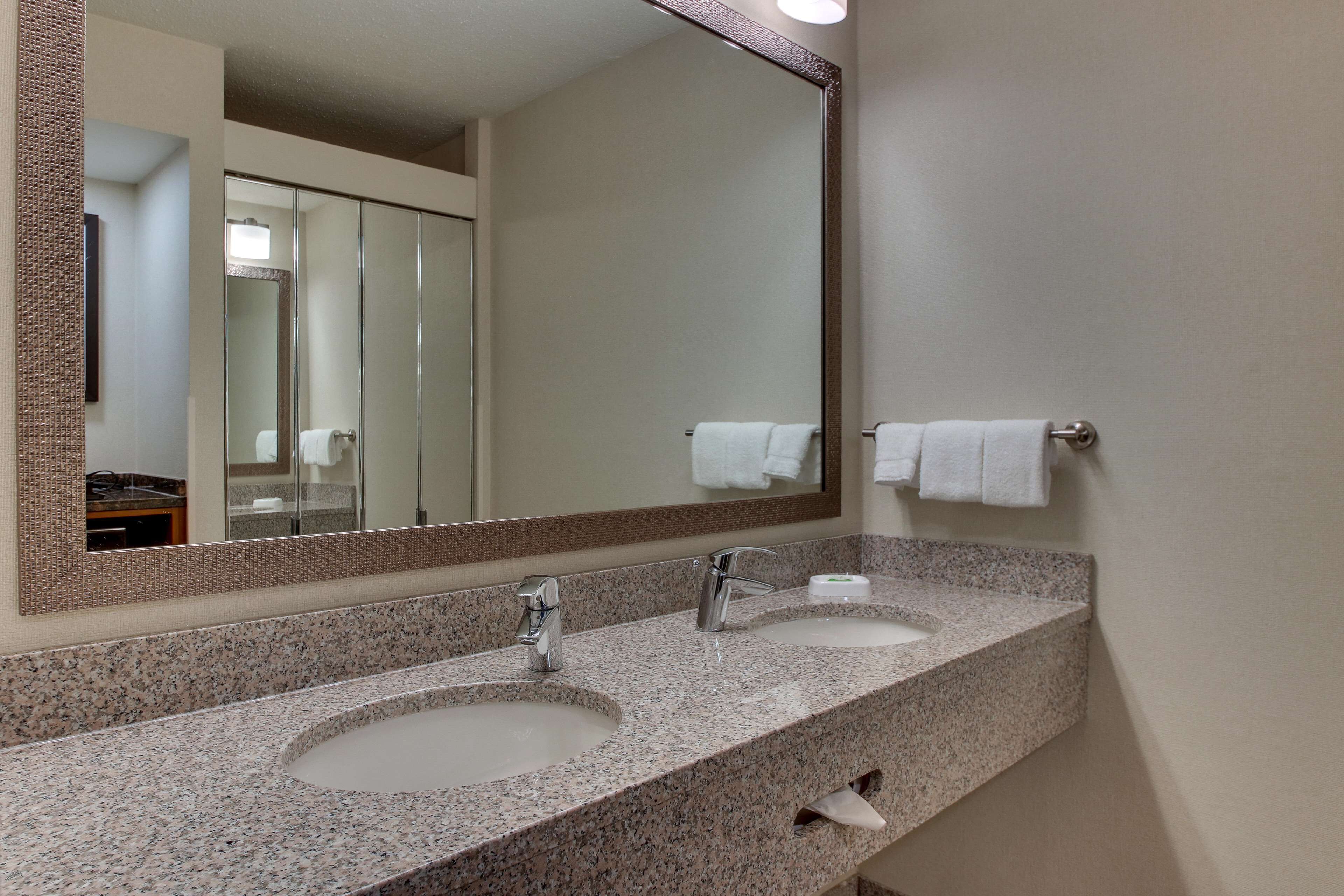 Un baño con dos lavamanos, un espejo grande y un perchero para toallas.