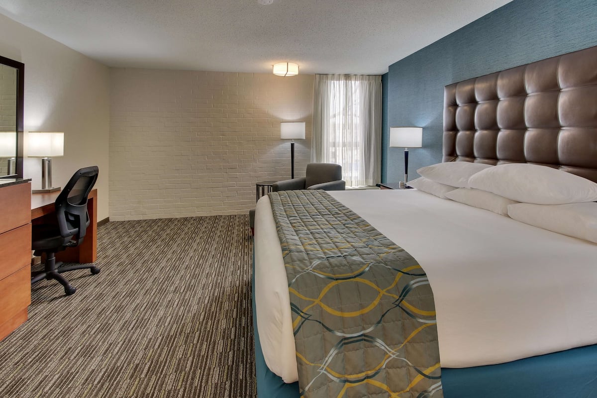 Ein Hotelzimmer mit einem großen Bett, einem Schreibtisch mit Stuhl, einer Lampe und einem Fenster mit Vorhängen.