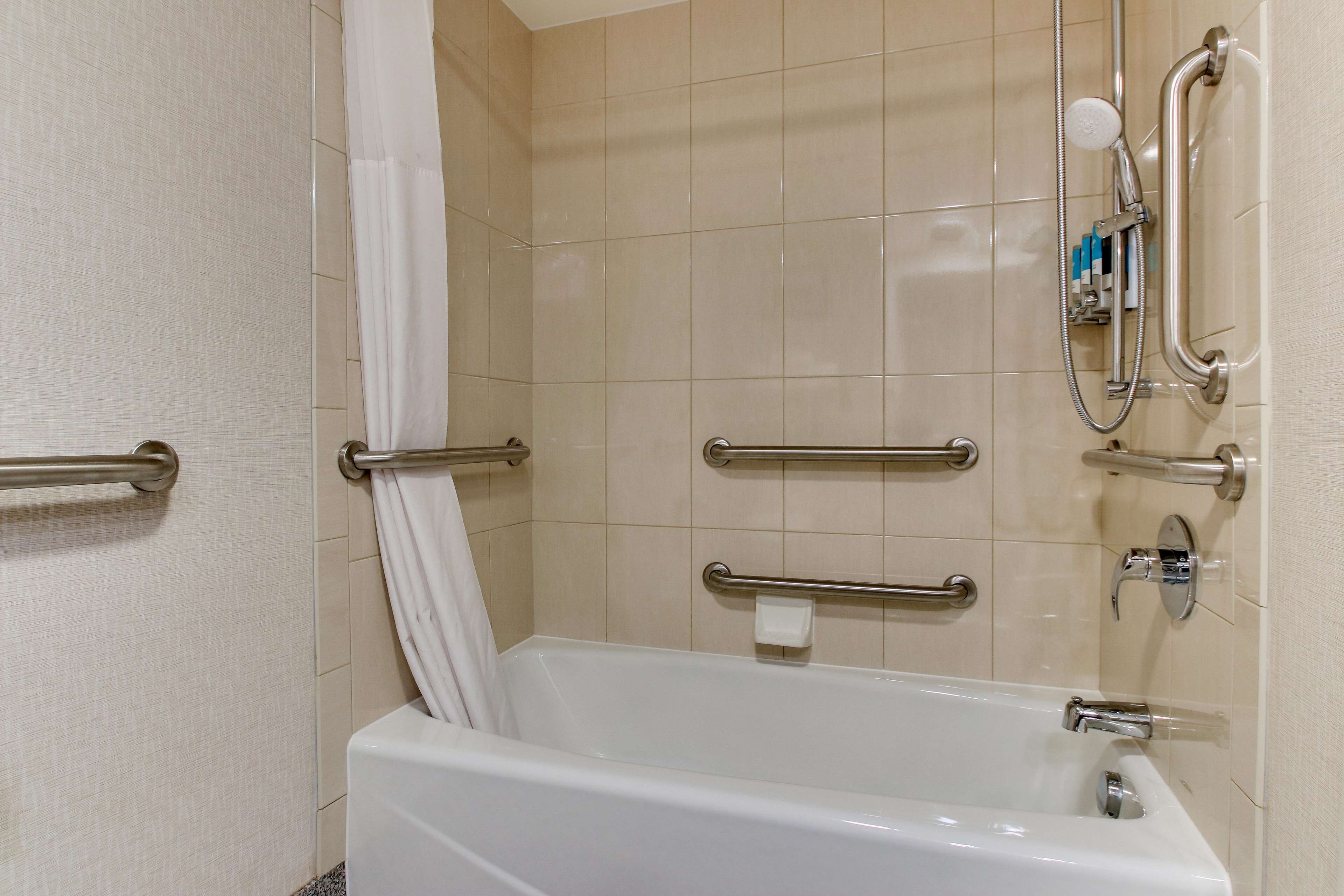 Un baño con bañera, barras de apoyo, cabezal de ducha y toallero.