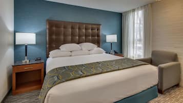 Habitación de hotel con una cama grande, dos mesitas de noche, una silla y una ventana con cortinas.