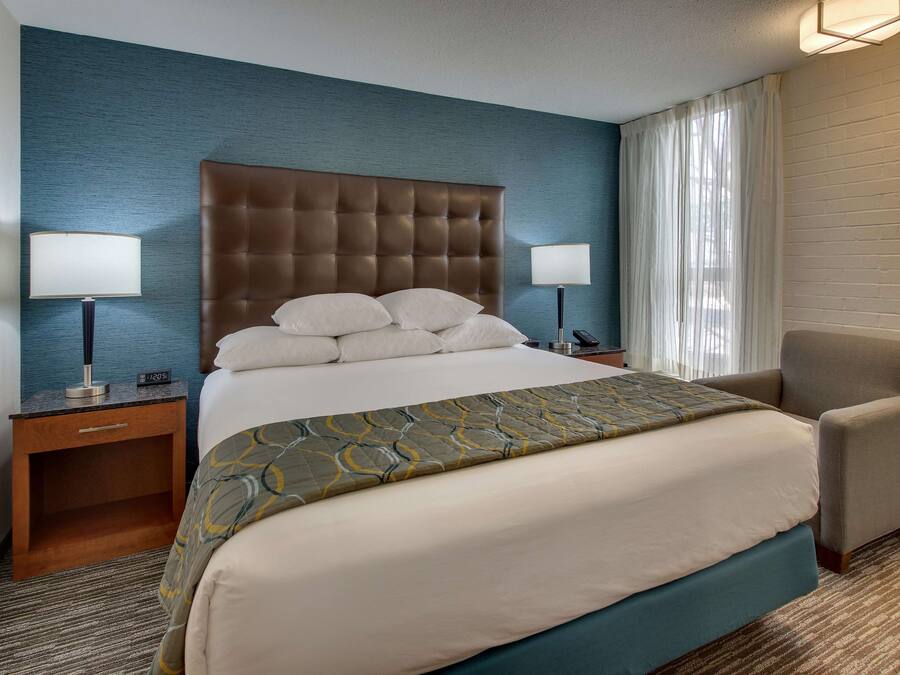 Une chambre d’hôtel avec un grand lit, deux tables de chevet, une chaise et une fenêtre avec des rideaux.