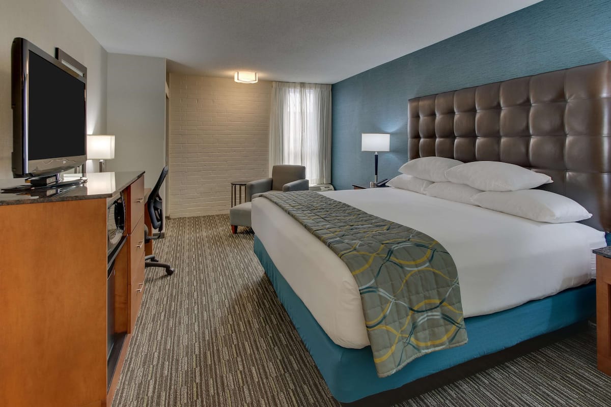 Ein Hotelzimmer mit einem großen Bett, einem Schreibtisch, einem Flachbildfernseher, einem Sessel und einer Lampe.