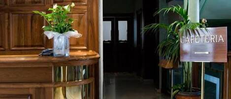 A reception area with a wooden reception desk, a sign reading "CAFETERIA", and potted plants.