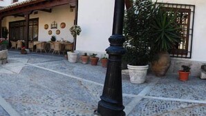 Un patio con suelo de baldosas, mobiliario exterior, plantas en macetas y un farol negro.