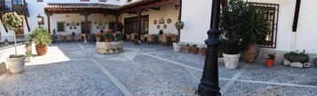Un patio con suelo de baldosas, mobiliario exterior, plantas en macetas y un farol negro.