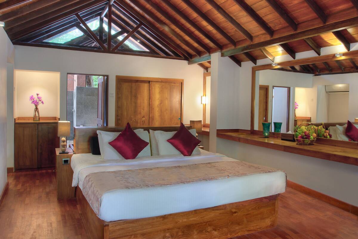 Een slaapkamer met een houten bed, een nachtkastje, een spiegel en een houten kledingkast.
