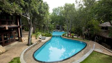 A swimming pool with a curved design, surrounded by a grassy area and trees.