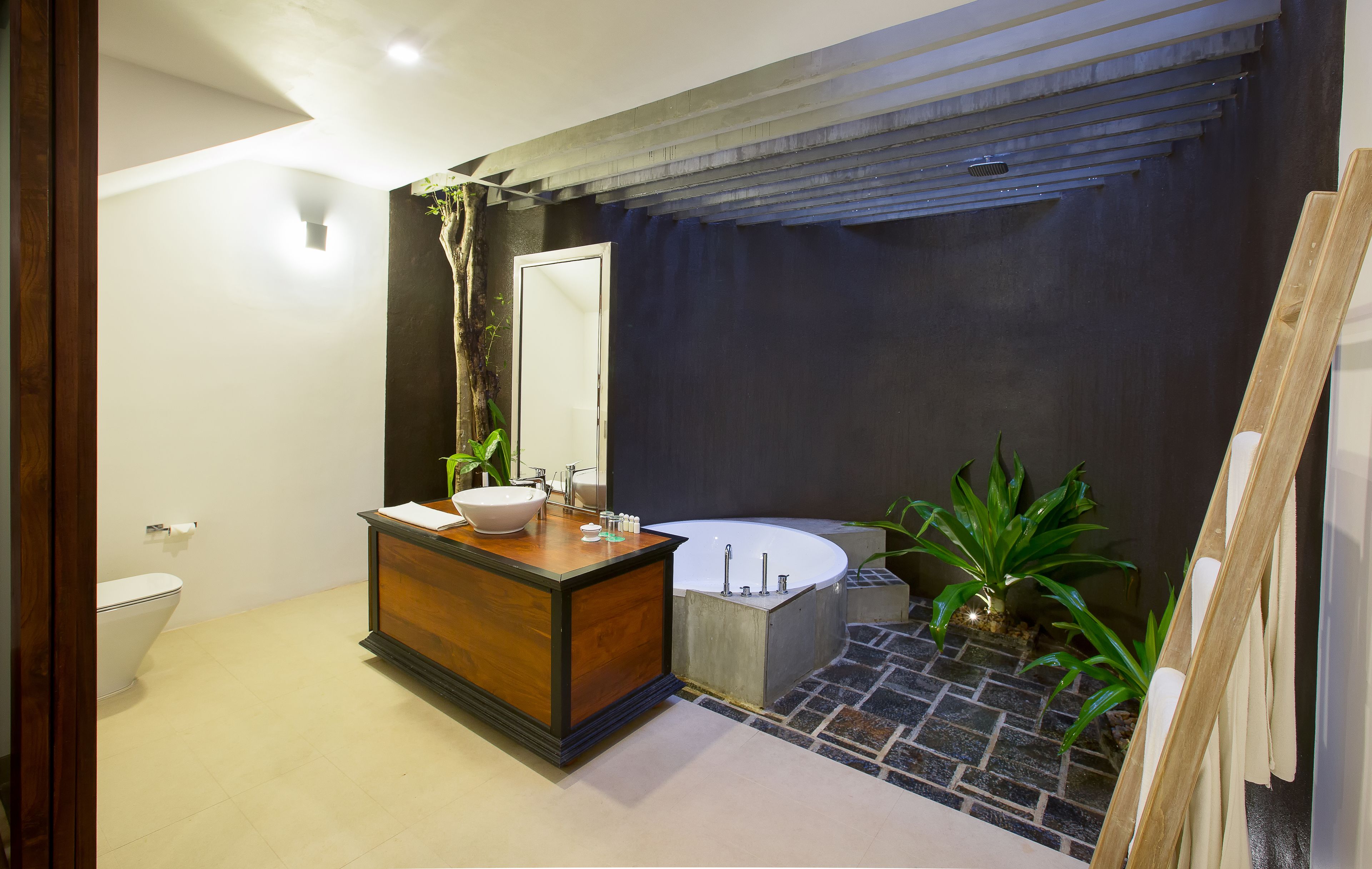 Un baño moderno con tocador de madera, un lavamanos blanco, una bañera grande y una pequeña planta verde.