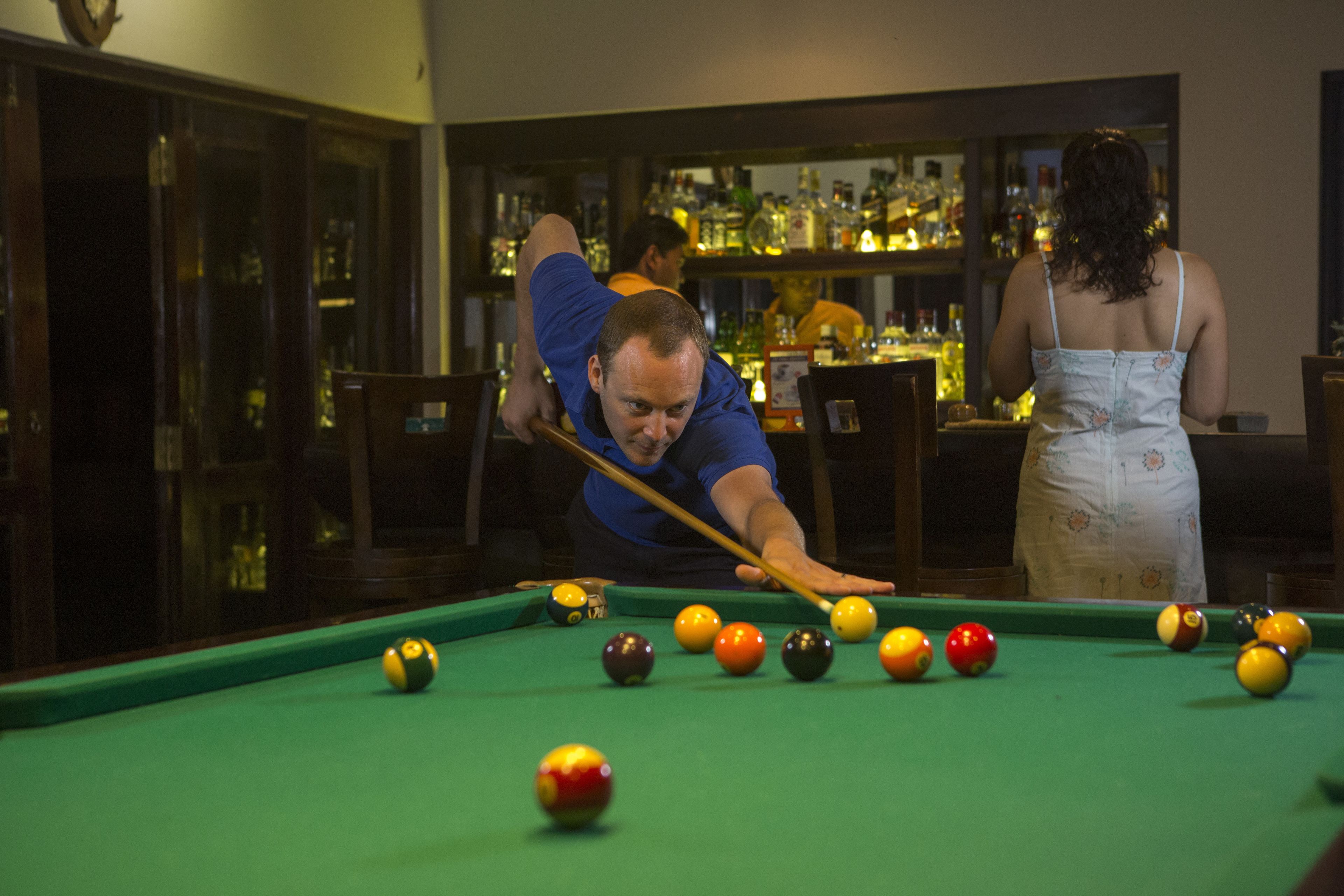 A pool table with balls, a bar area with bottles, and a person playing pool.