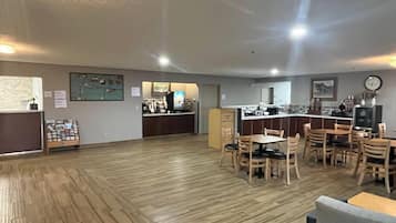 Una habitación amplia con piso de madera, una zona de cocina con mostrador y sillas, y un comedor con mesas y sillas.