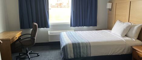 A hotel room with a bed, a desk, a chair, and a window with curtains.