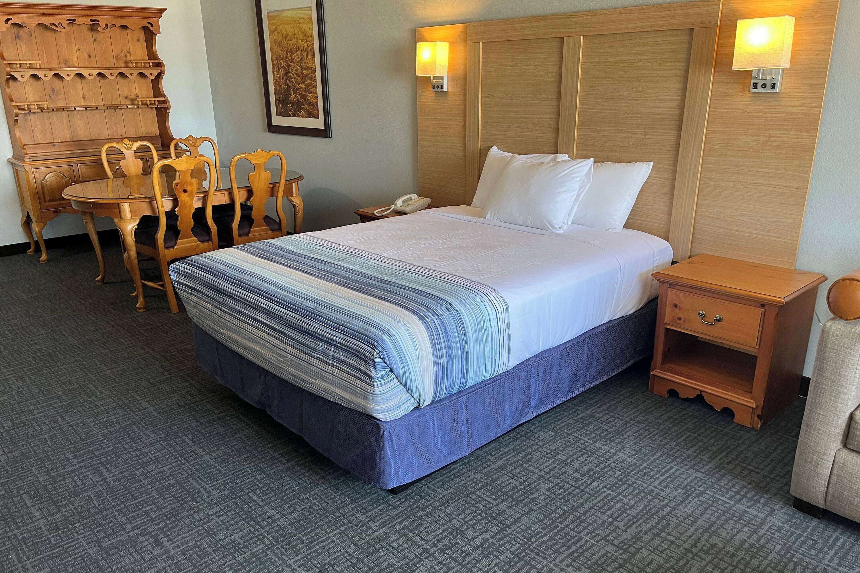 Une chambre d’hôtel avec un grand lit, une tête de lit en bois, une table de chevet et un bureau avec des chaises.