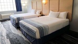 A hotel room with two beds, a large window with curtains, a wall-mounted light, and a rug. - Days Inn & Suites by Wyndham Williamsburg IA North (Williamsburg)