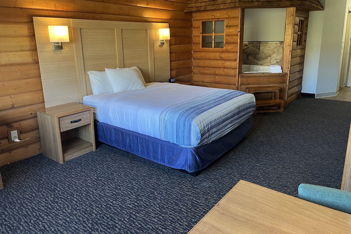 A wooden cabin-style room with a bed, bedside table, and a small bathroom with a sink and mirror.