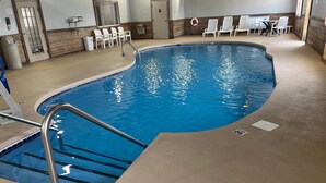 An indoor swimming pool with a curved edge, a metal ladder, and white chairs around the perimeter. - Days Inn & Suites by Wyndham Williamsburg IA North (Williamsburg)