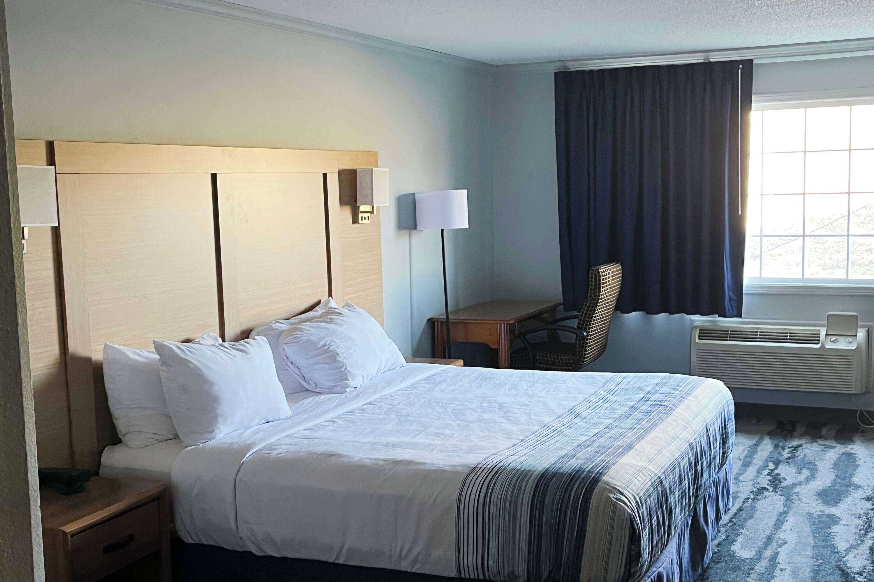 Una habitación de hotel con una cama grande, lámparas de noche, un escritorio, una silla y un equipo de aire acondicionado.