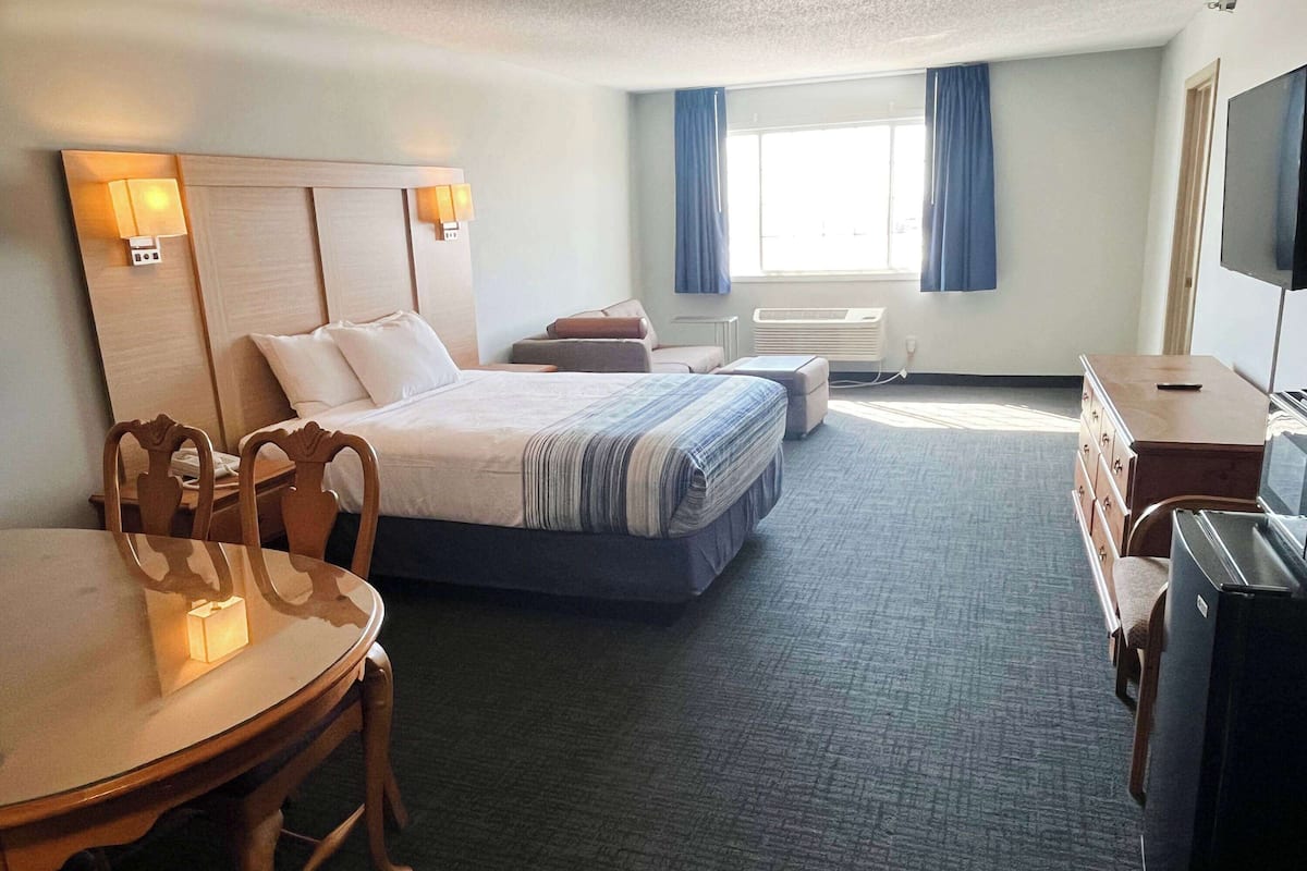 A hotel room with a bed, a desk, a chair, a television, and a window with curtains.