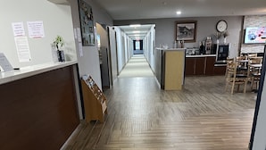 A hotel corridor with wooden flooring, a reception desk, and a dining area with chairs and tables. - Days Inn & Suites by Wyndham Williamsburg IA North (Williamsburg)