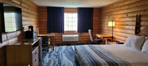 Ein Blockhauszimmer mit Bett, Schreibtisch, Stuhl, Fernseher und einem Fenster mit Vorhängen.