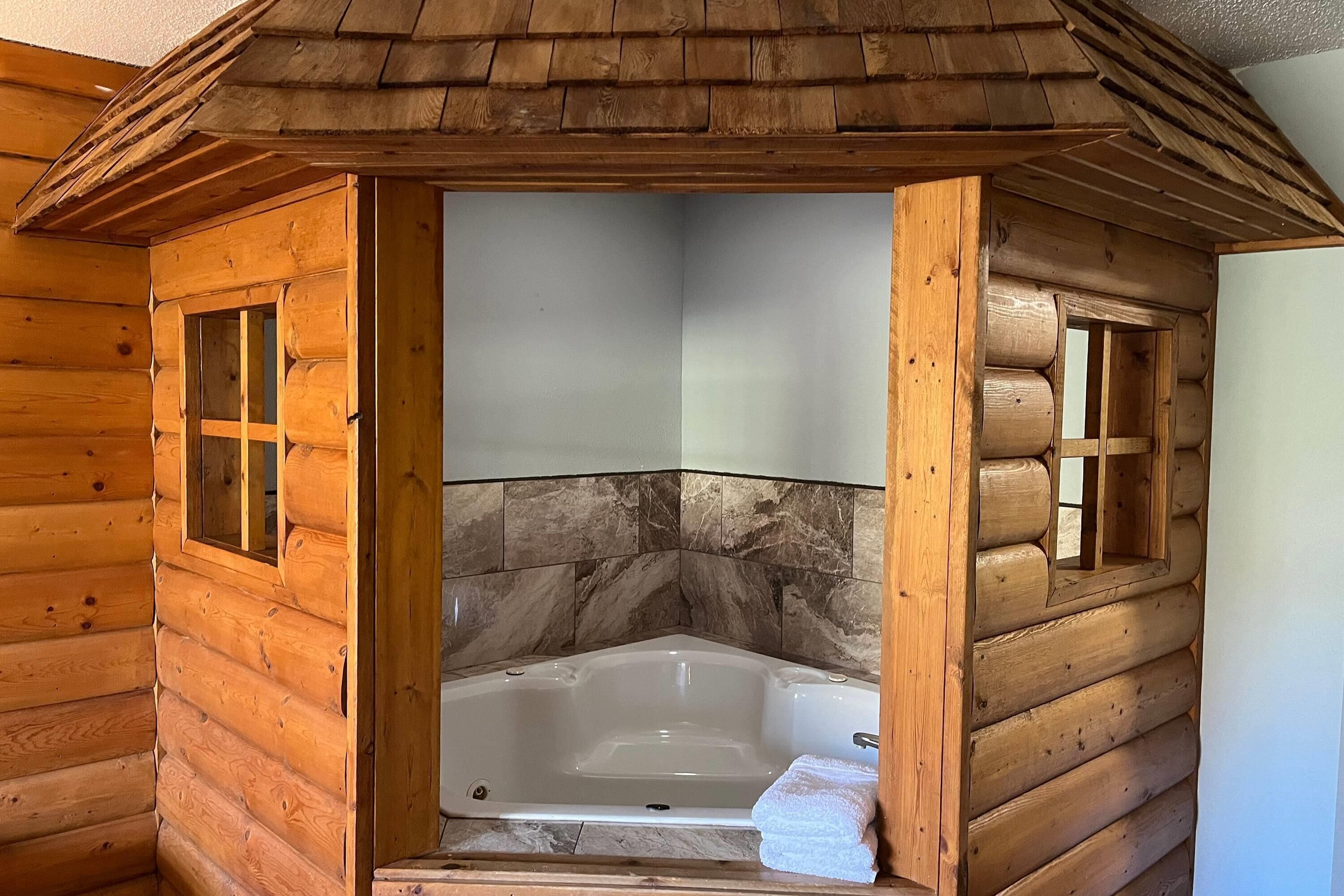 A log cabin bathroom with a wooden exterior, a marble-tiled shower wall, and a bathtub.
