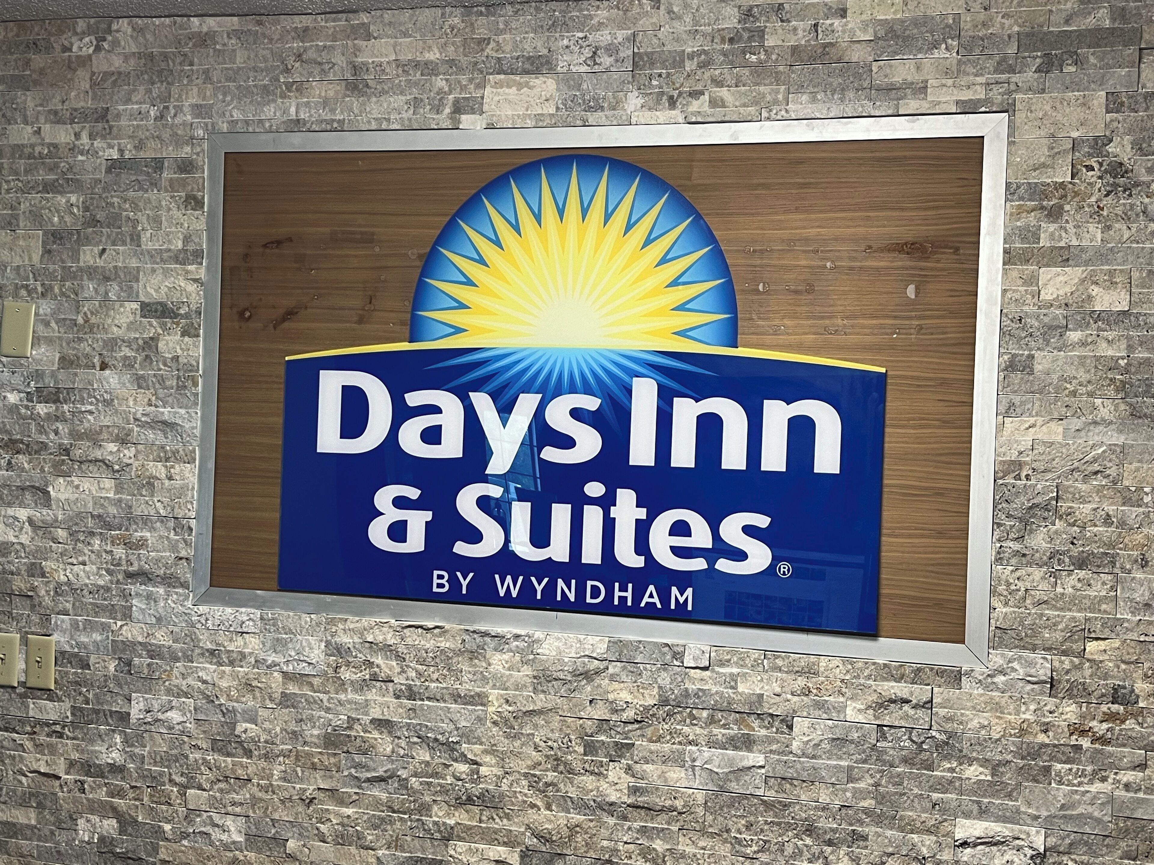 A sign for Days Inn & Suites by Wyndham, featuring a sunburst logo and a wooden background.
