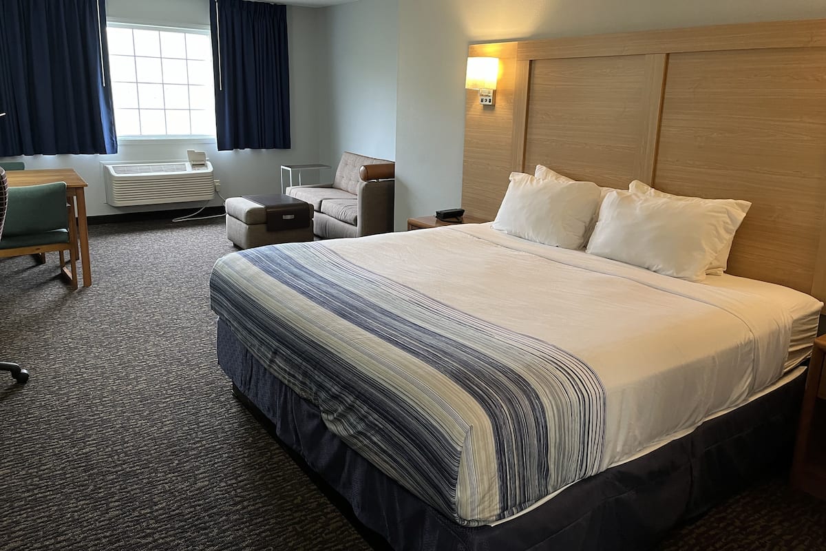 A hotel room with a large bed, a desk, a chair, a sofa, and a window with curtains.
