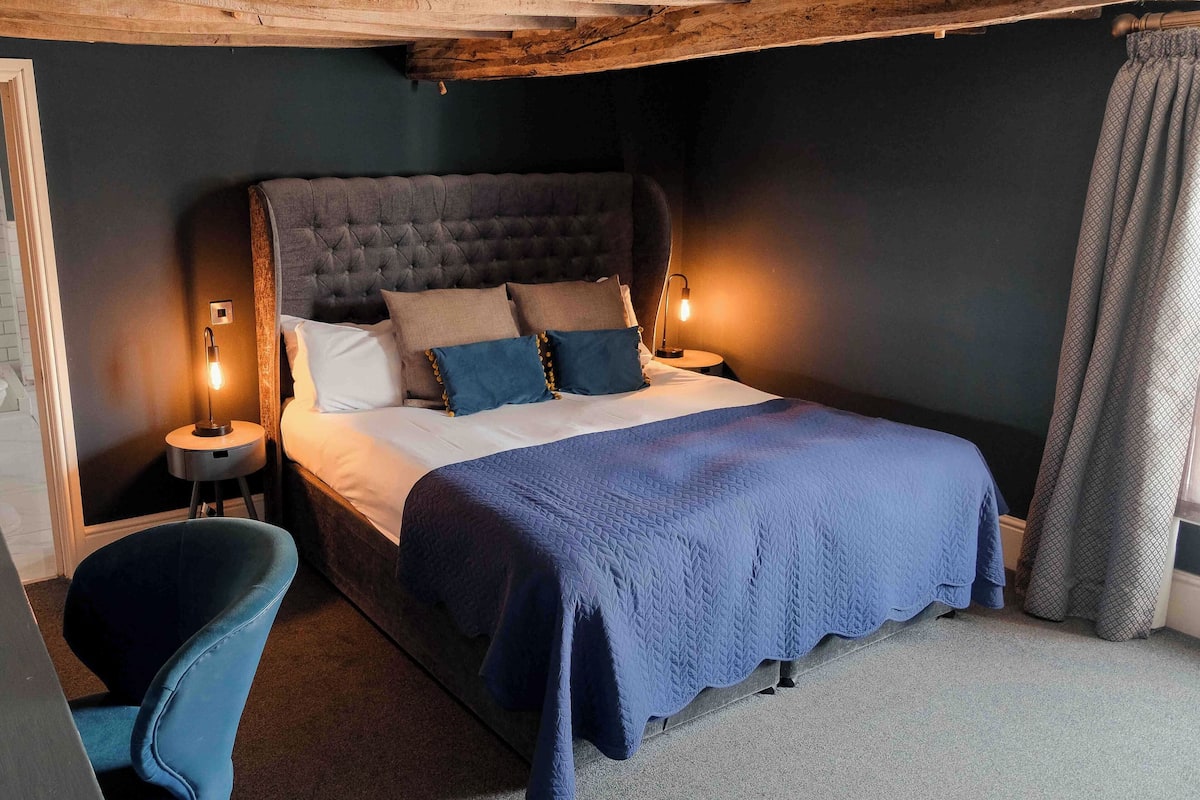 A bedroom with a large bed, two bedside lamps, a blue chair, and a wooden ceiling.