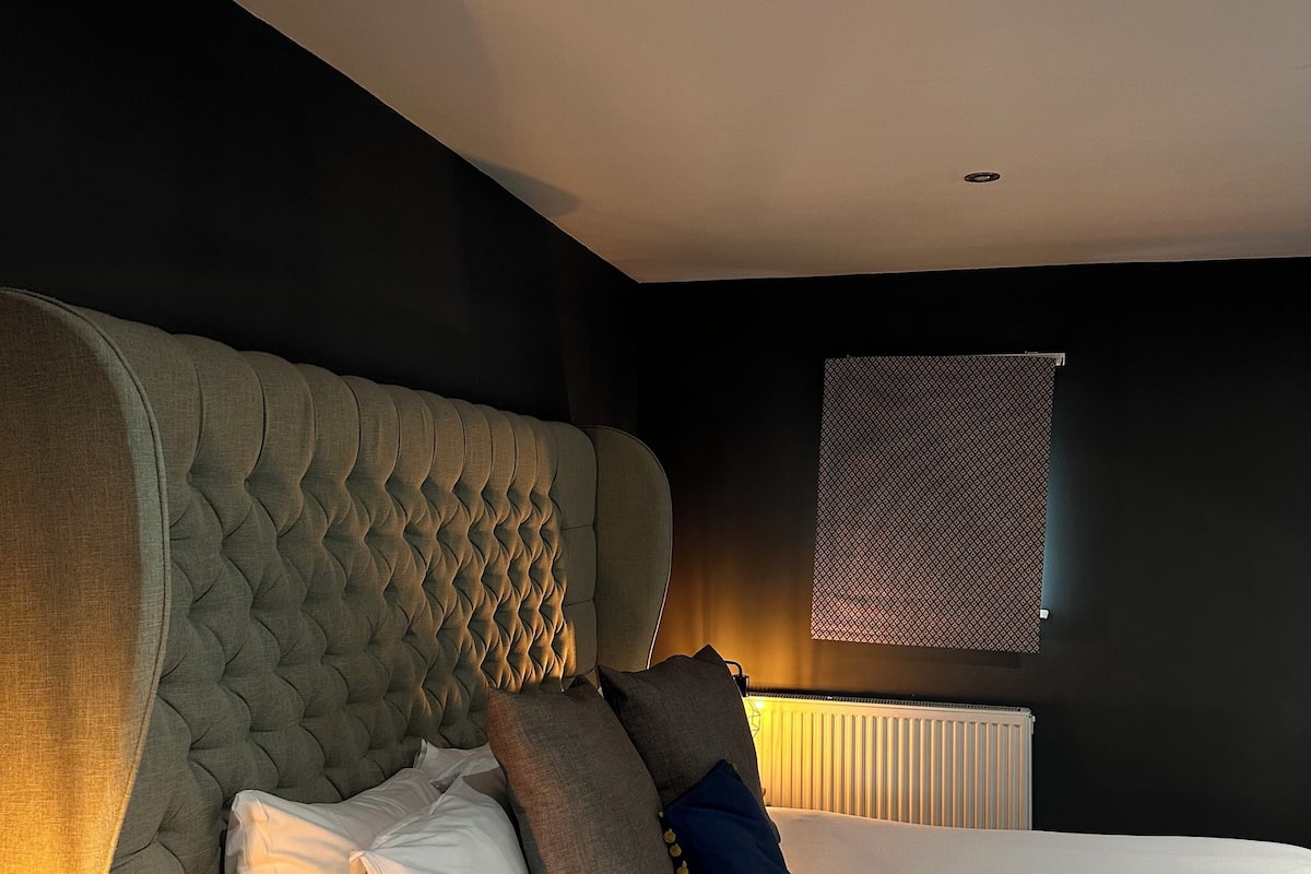 A bedroom with a large tufted headboard, a white bedspread, and several pillows.