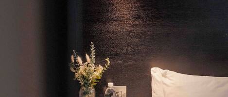 A bedroom with a bed, a nightstand, a lamp, a vase with flowers, and a bottle.