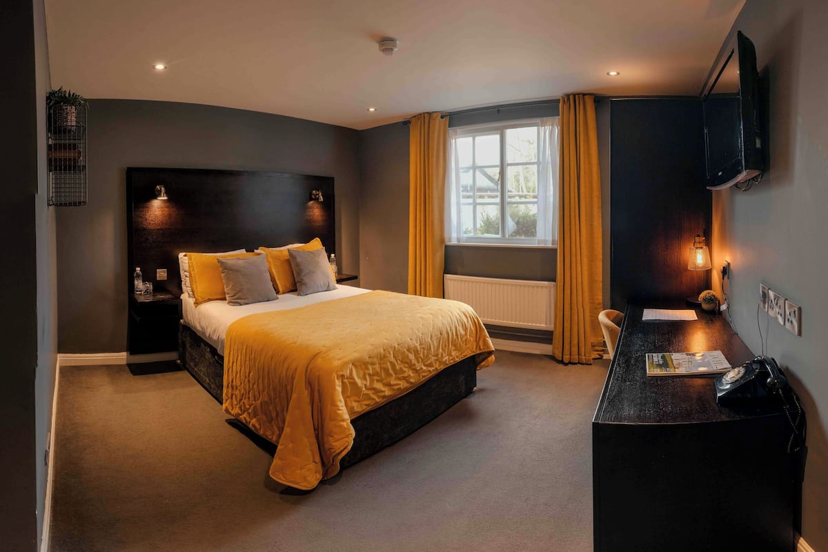 A hotel room with a bed, bedside table, desk, and a television mounted on the wall.