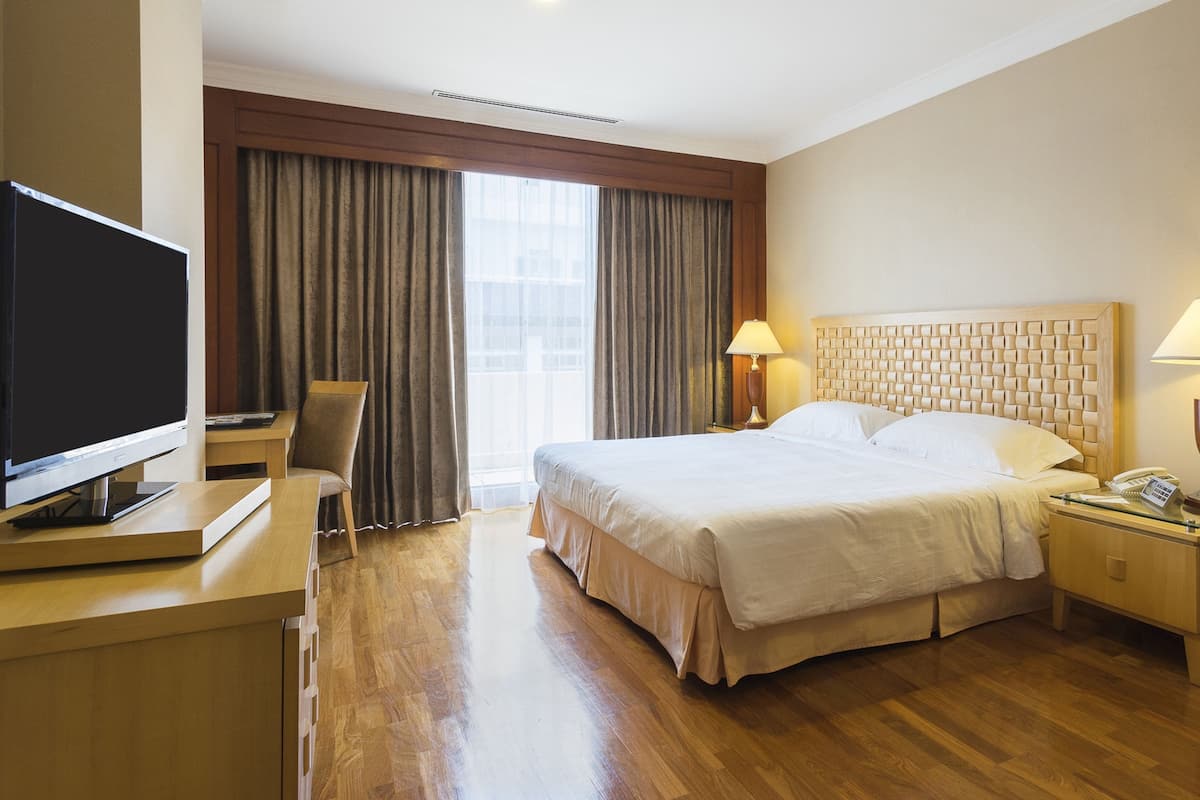 A hotel room with a large bed, a desk with a TV, two bedside lamps, and a window with curtains.