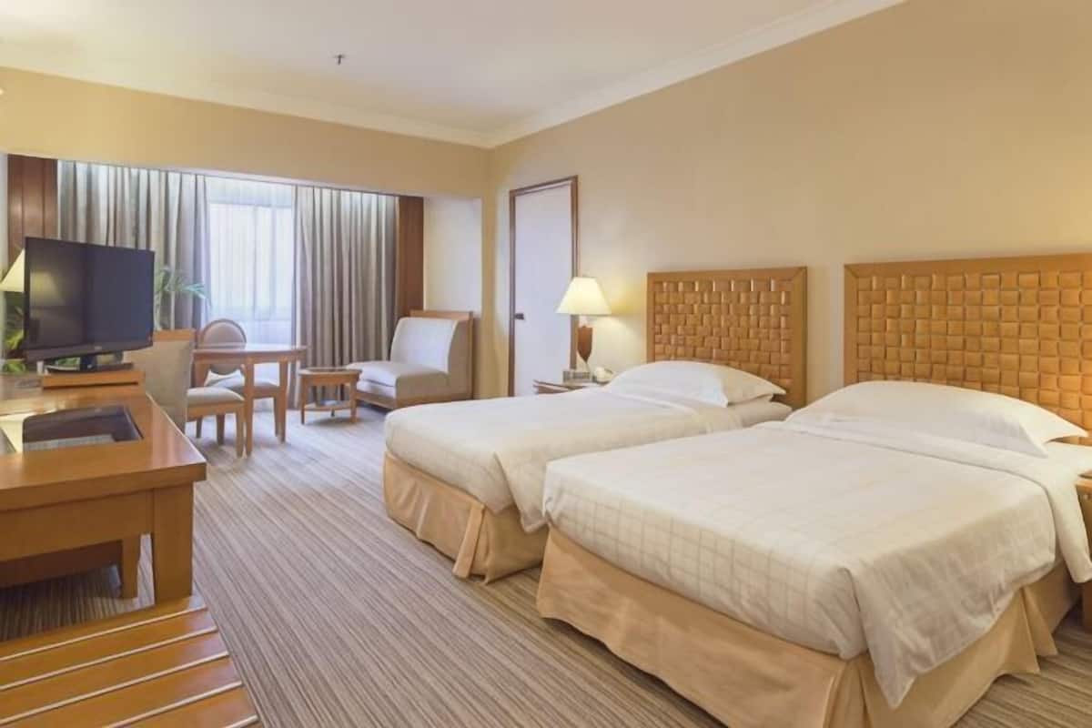 A hotel room with two beds, a desk with a TV, a chair, and a lamp.