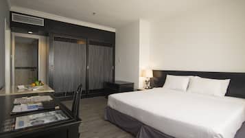 A hotel room with a large bed, a desk with a chair, a small table with a lamp, and a wardrobe.