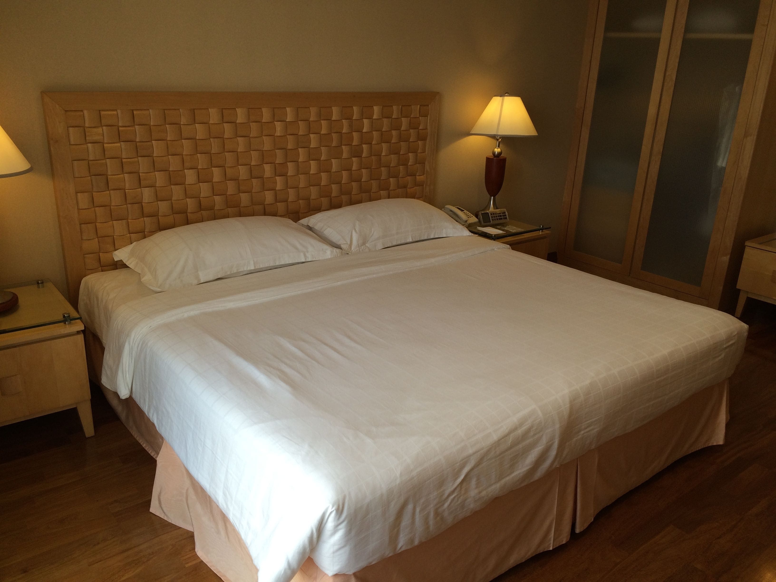 Una cama bien hecha con un cabecero de madera, dos mesitas de noche con lámparas y suelo de madera.