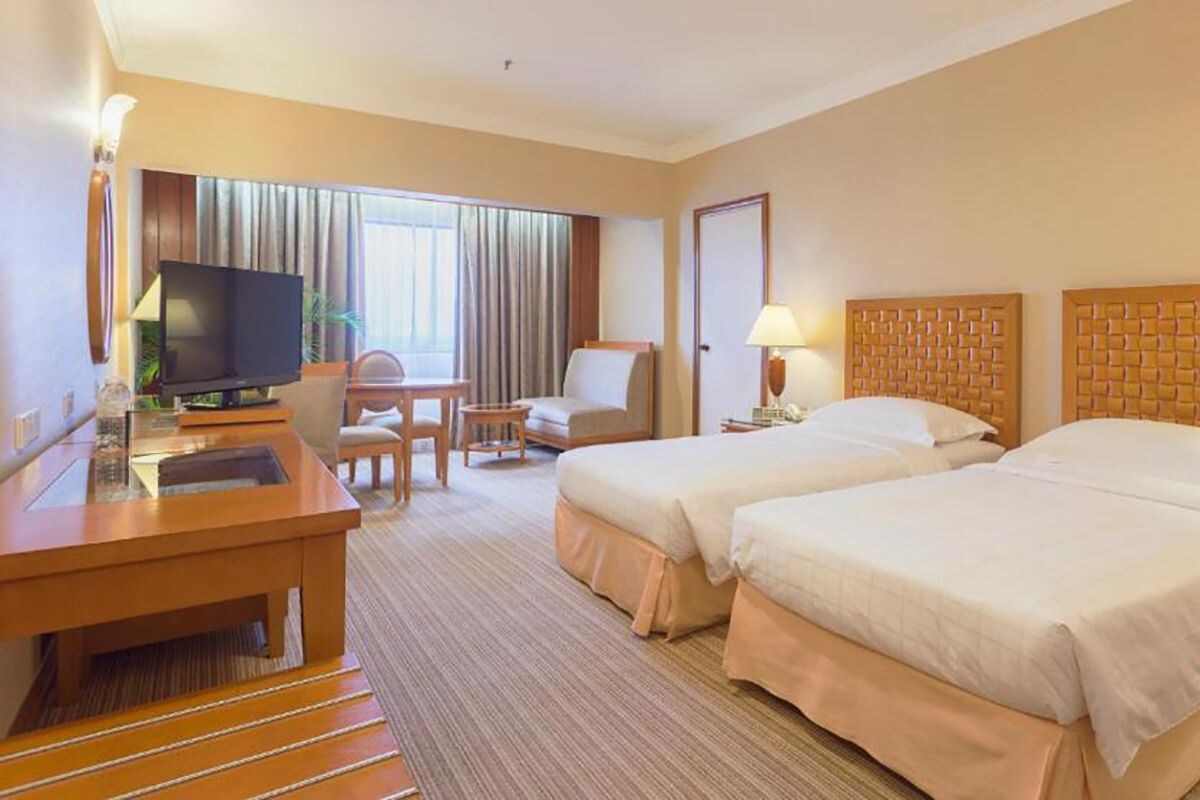Una habitación de hotel con dos camas, televisión, escritorio y una silla.