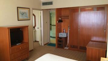 Habitación de hotel con cama, armario de madera, televisor y baño con ducha, además de un cuadro en la pared.