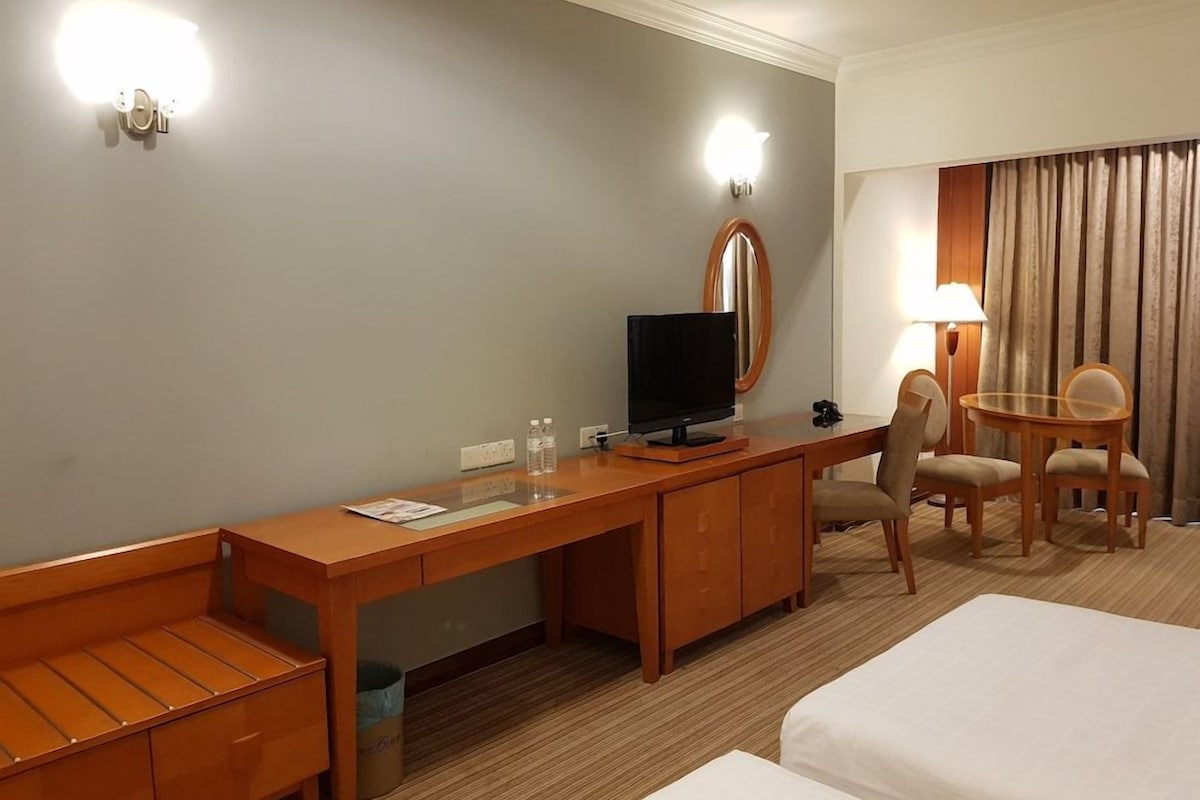 Una habitación de hotel con un escritorio de madera, televisor, una silla, una cama y una lámpara.