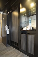 A modern hotel room with a dark wood finish, a glass partition, and a small kitchenette area.