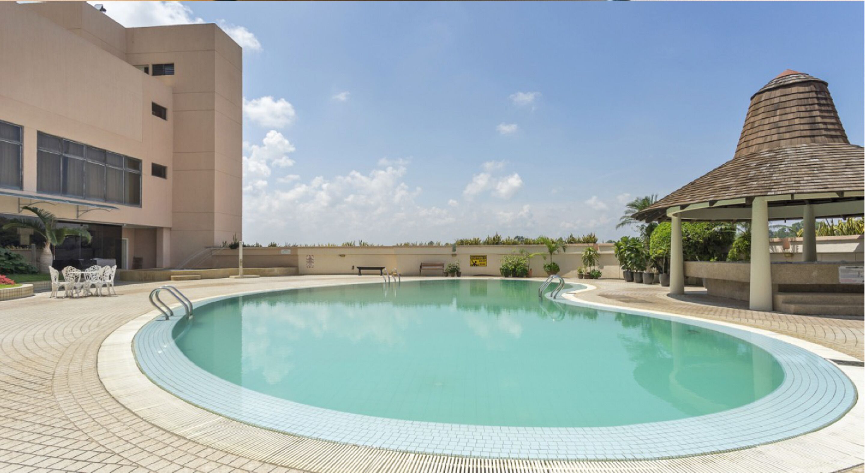 A swimming pool with a tiled deck, a gazebo, and a building with large windows.