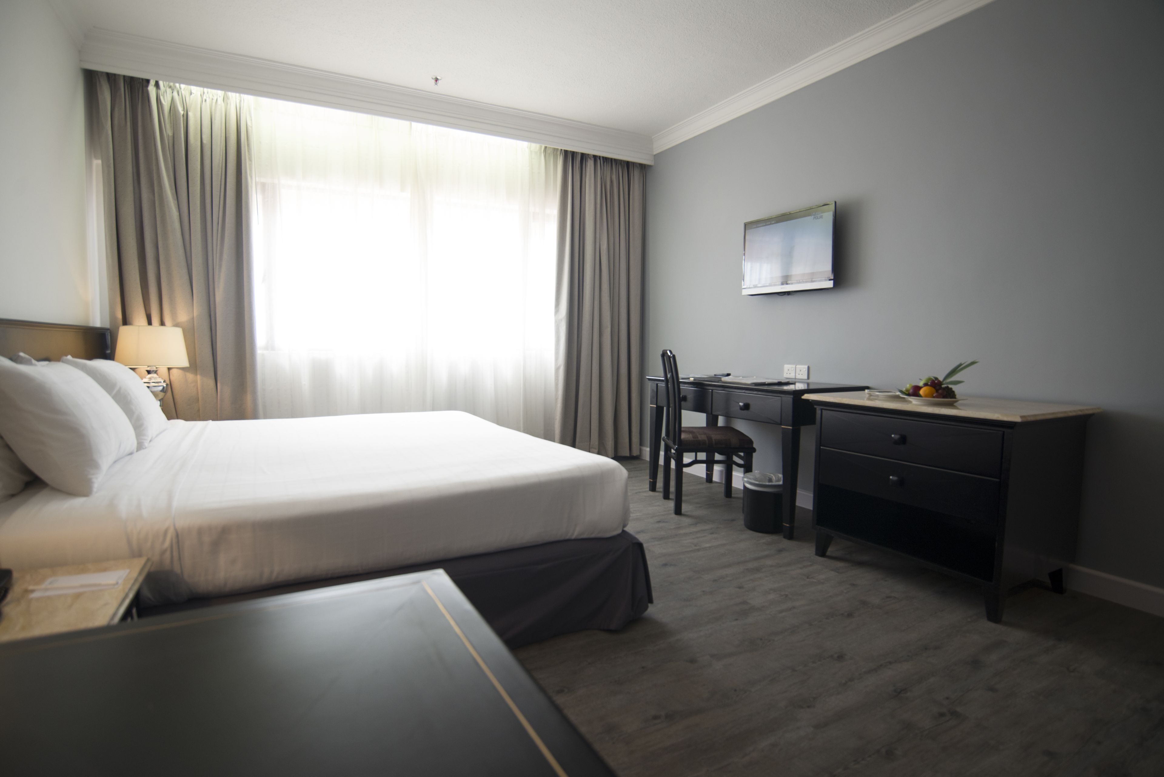 Habitació d'hotel amb llit, escriptori, cadira, televisió i finestra amb cortines.