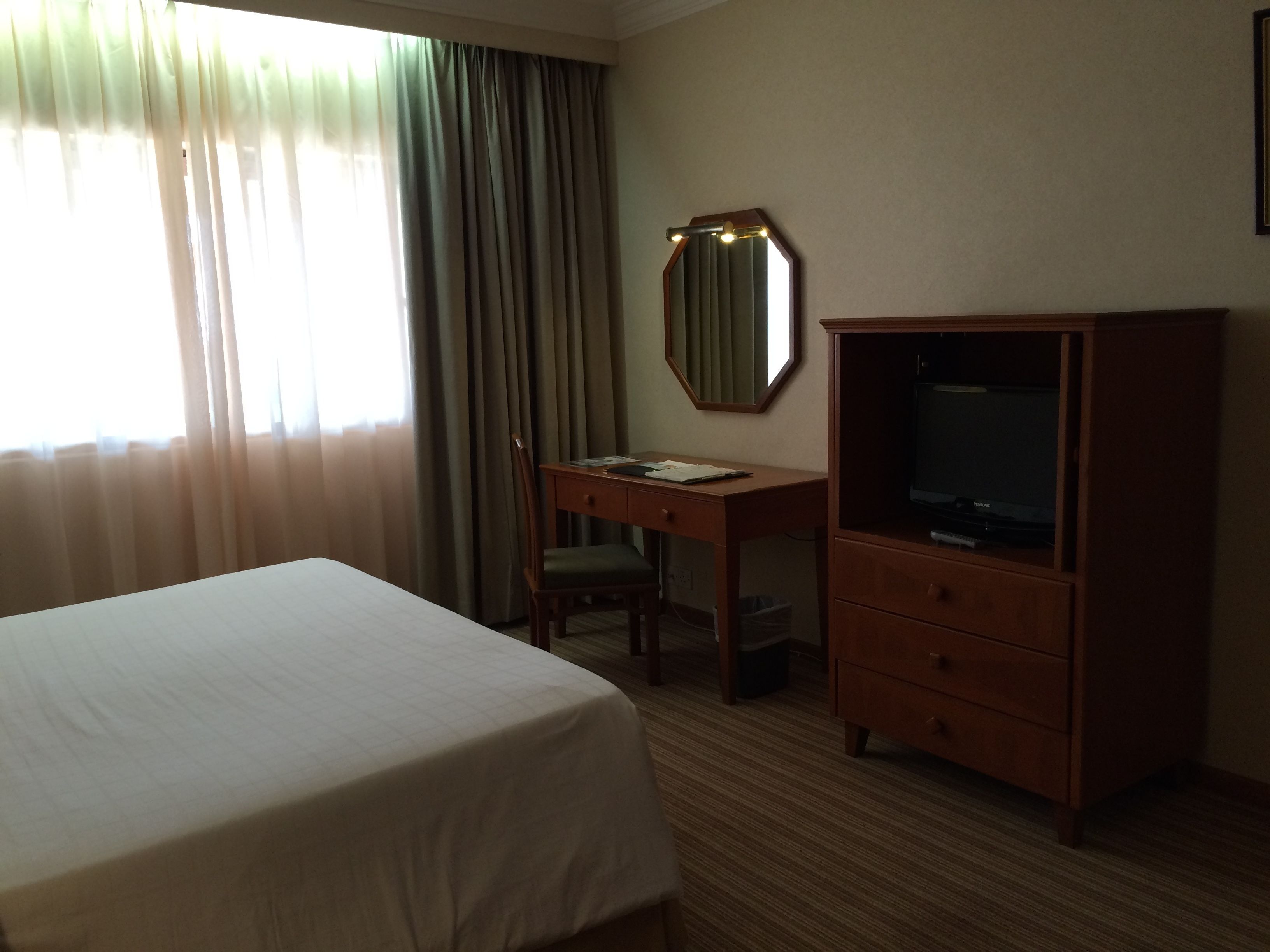 A hotel room with a bed, a desk with a chair, a television, and a mirror.