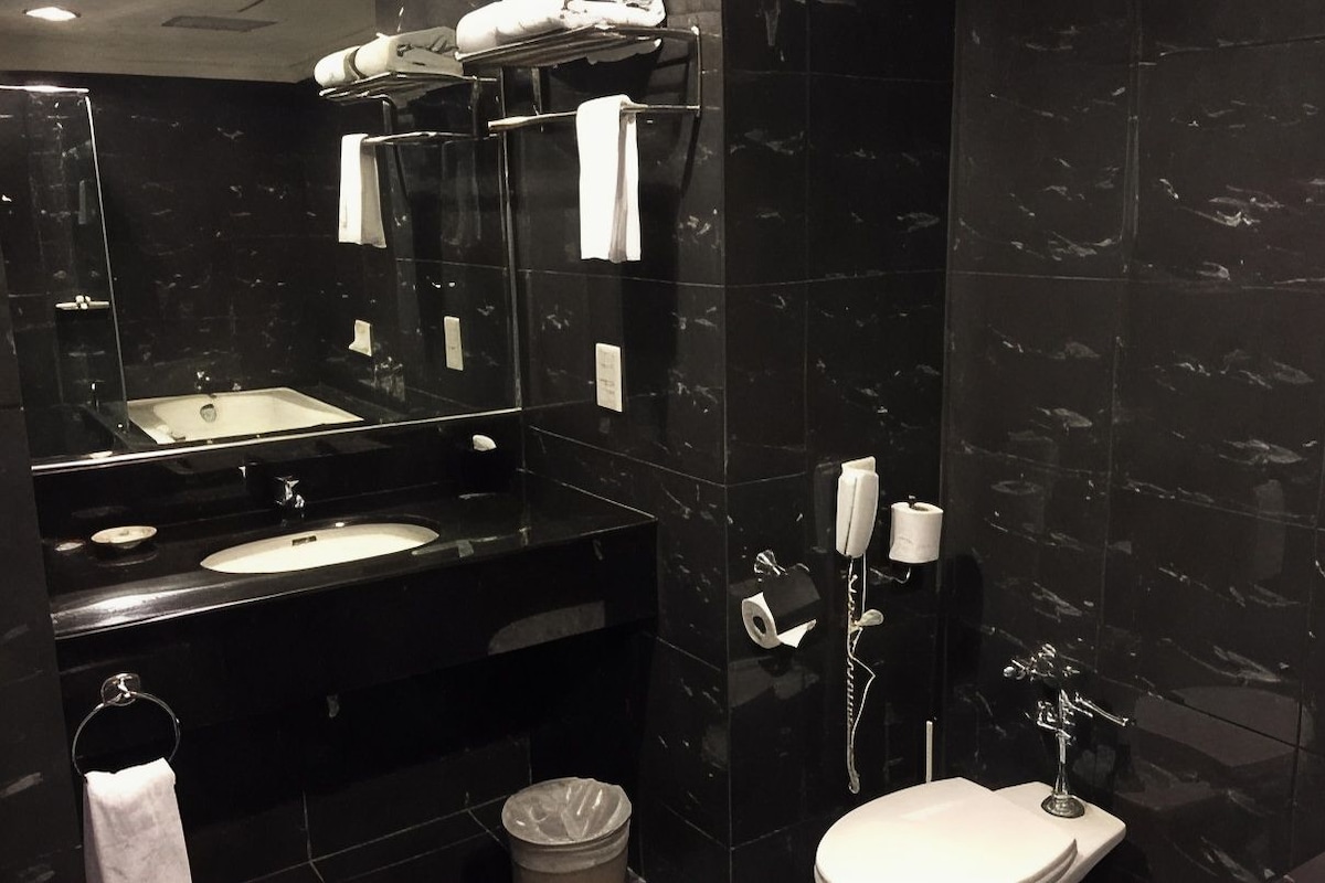 Un baño moderno con lavamanos de mármol negro, ducha con cerramiento de vidrio y un inodoro blanco.
