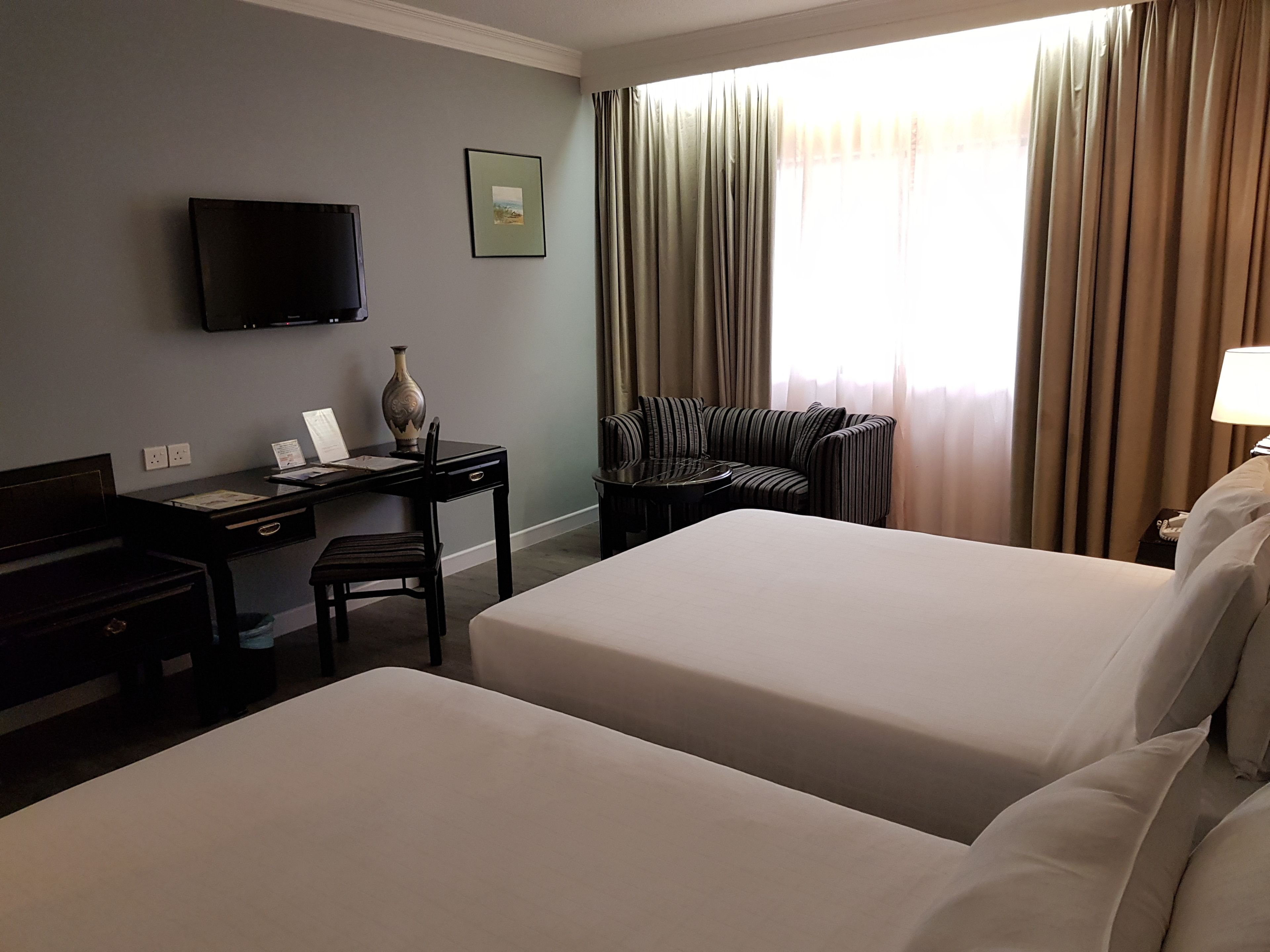 A hotel room with two beds, a desk with a chair, a television mounted on the wall, and a window with curtains.