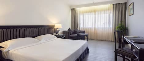 A hotel room with a large bed, a desk, a chair, a lamp, and a window with curtains.