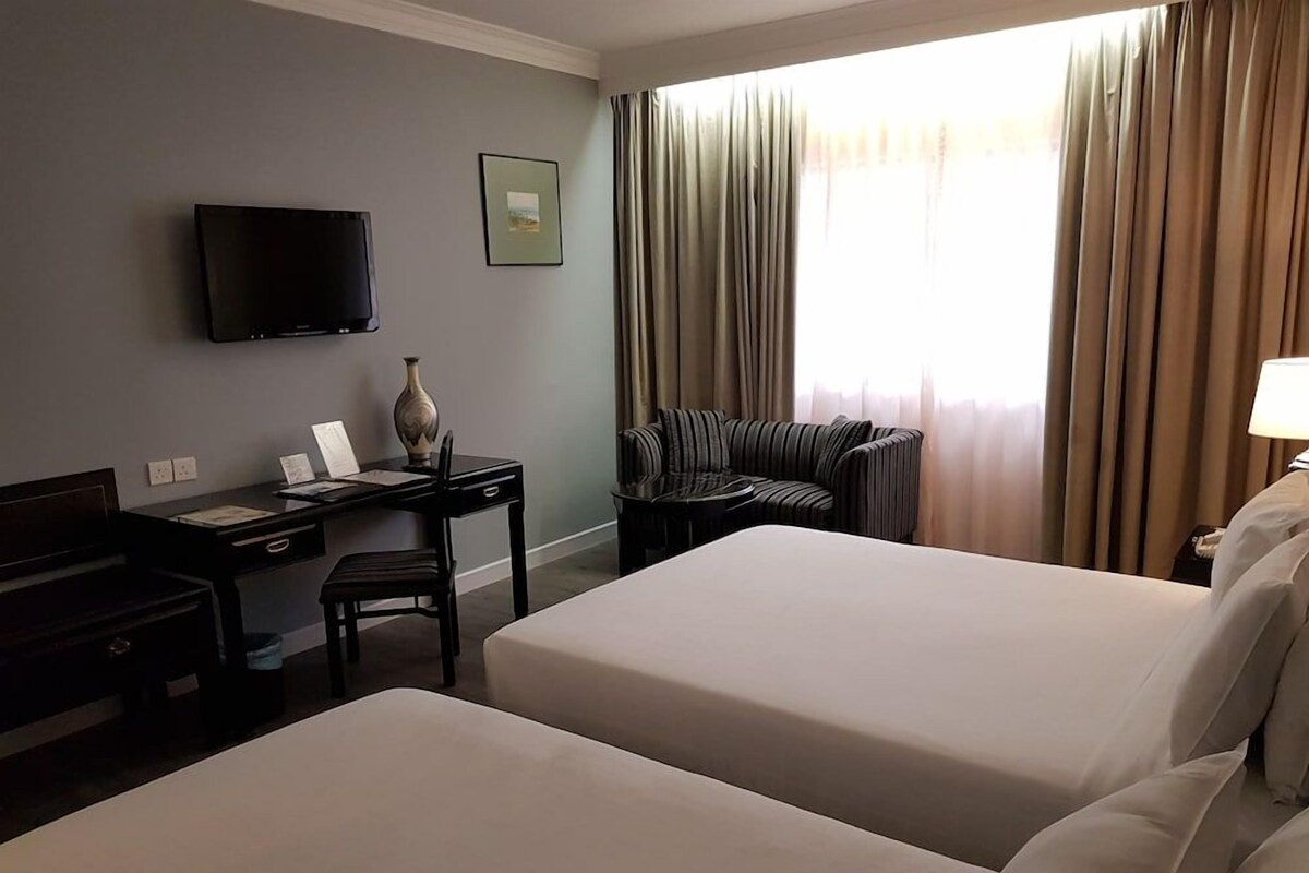 Habitación de hotel con dos camas, un escritorio con silla, un televisor en la pared y una ventana con cortinas.