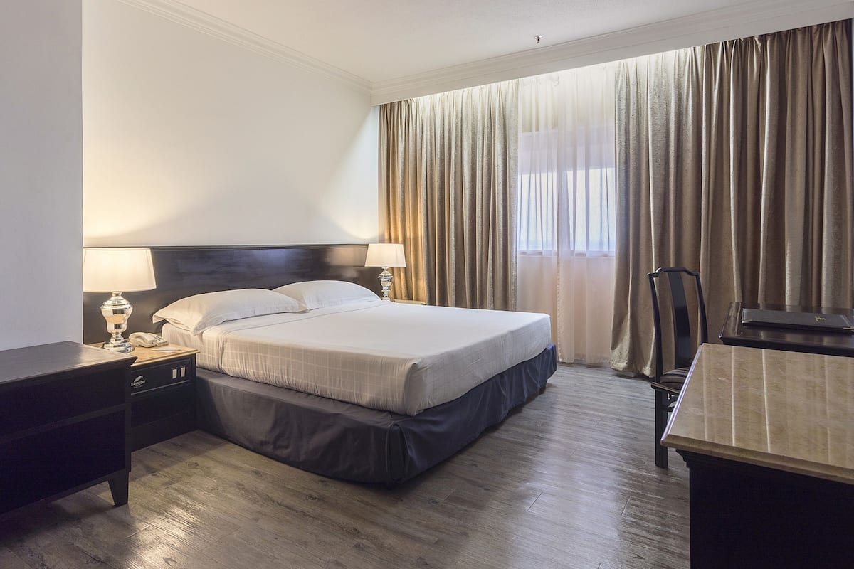 A hotel room with a bed, bedside tables, a desk, and a large window with curtains.